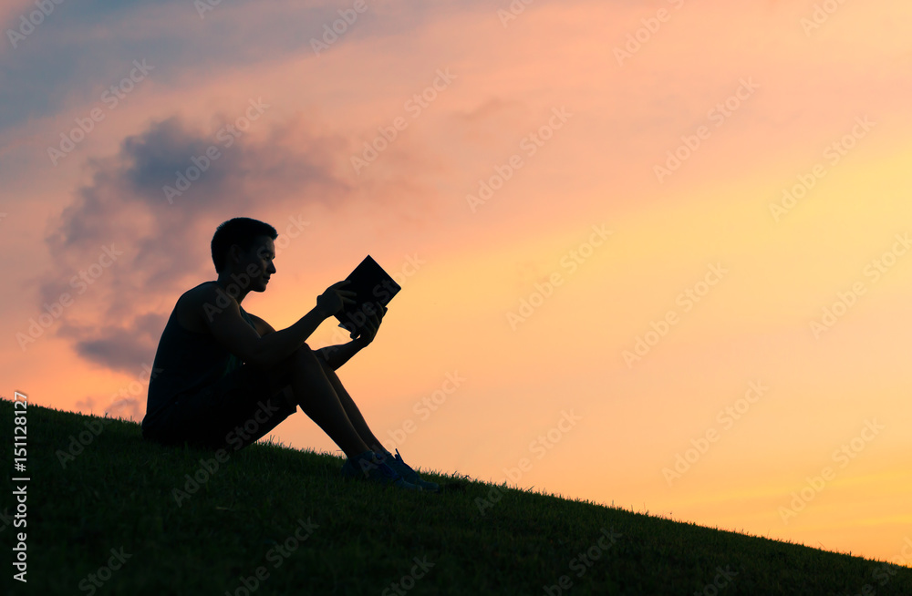 Silhouettes of young man reading a book.